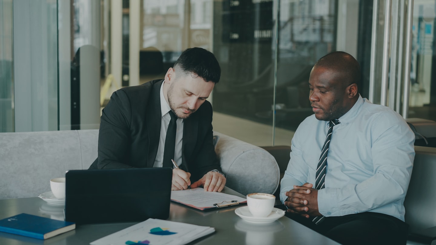 Man in suit signs document while colleague watches.